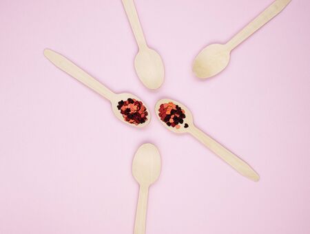 Eco-friendly biodegradable compostable wooden spoons on a soft pink background. Red confetti hearts on spoons. Background for the holidaysの写真素材
