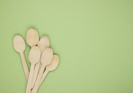 Eco-friendly disposable tableware made of bamboo wood and paper on a green background. Draped spoons...