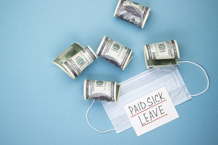 Medical mask with dollars and the words paid sick leave on a blue background. Concept of economic...