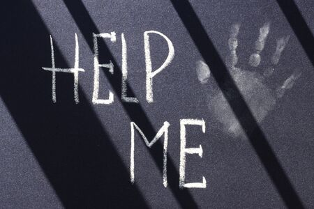 help me inscription in white chalk trace of a child's hand on a black surface. request for helpの写真素材