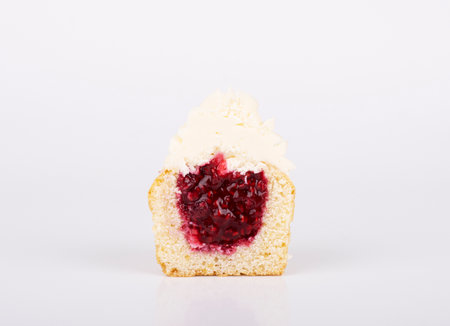 The cupcake is cut in half, with cherry filling and white vanilla icing. biscuit side viewの写真素材