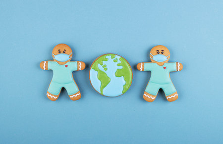 two gingerbread man medics in a mask with the gingerbread planet earth on a blue background. the concept of a worldwide coronavirus pandemicの写真素材