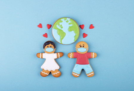 Gingerbread boy and girl in medical masks, lots of little red hearts and planet earth. Valentine's day during the worldwide coronavirus pandemicの写真素材
