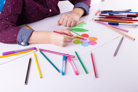 The boy draws a flower with colored pencils and markers on white paper. children's drawings, children's creativityの写真素材
