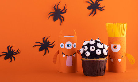 Paper ghost, a scary handmade monster with a black cupcake on an orange background with black spiders. The concept of Halloween crafts, DIY, creative toilet tubeの写真素材