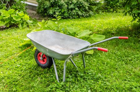 garden trolley with red handles and wheels stands on the grassの写真素材