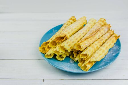 homemade waffle tubes on a blue plate on white background with copy space