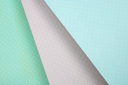 Colored paper background is a delicate pastel, blue, mint and pink in white polka dots. diagonally,...