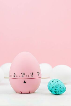 pink kitchen egg timer on a pink background. cooking time, soon Easter. white hen eggs and blue quail egg. copy spaceの写真素材