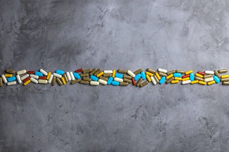 Top view of multi-colored medical capsules and pills on a gray concrete background. The concept of...