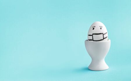egg in mask in an egg stand on blue background. concept of Easter, disease, virus prevention with...