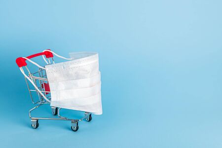 Shopping cart with protective medical mask against coronavirus. Safe and online shopping on quarantine concept.の写真素材