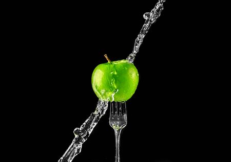 green fresh juicy apple on a fork in splashes of water on a black backgroundの写真素材