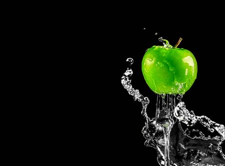 green fresh juicy apple on a fork in splashes of water on a black background with copy spaceの写真素材