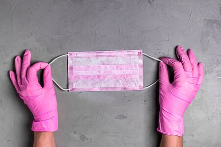 Women's hands in pink gloves hold pink medical disposable mask on grey background. Hands of woman with mask close-up. Top view, flat lay.の写真素材