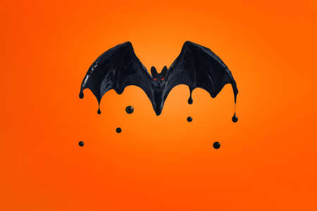 black bat with red eyes on an orange background. flowing black paintの写真素材