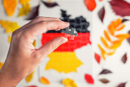 hand holds a piece of puzzle in the form of Germany in the colors of the German flagの写真素材