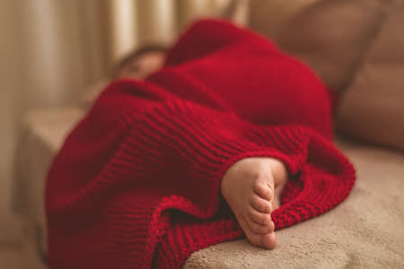 a cute girl in a red blanket on the couchの写真素材