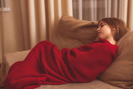 a cute girl in a red blanket on the couchの写真素材