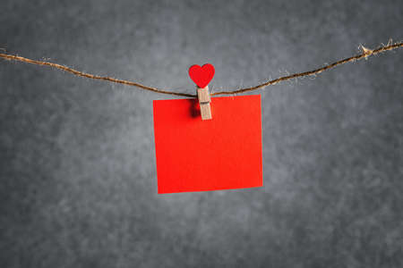 red piece of paper with a clothespin in the form of a heart on a gray backgroundの写真素材
