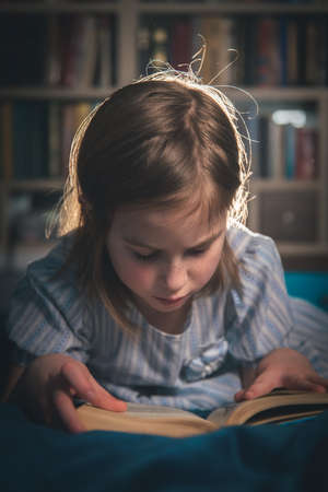 cute girl reading a book at home, lying on the bedの写真素材