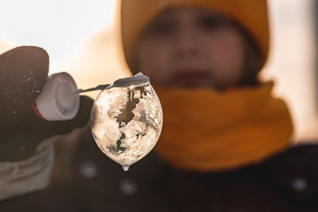 a girl holds a soap bubble with beautiful frost patterns in the rays of the sunの写真素材