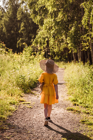 cute little girl in a yellow dress and straw hat walking through the forest
