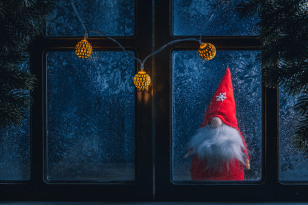 Christmas, new year, winter composition. Christmas Gnome behind a frozen window with frosty patternsの写真素材