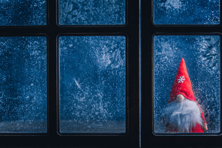 Christmas, new year, winter composition. Christmas Gnome behind a frozen window with frosty patternsの写真素材