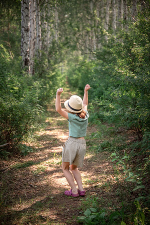 a cute girl in a straw hat walks along a path in the woods in the summerの写真素材