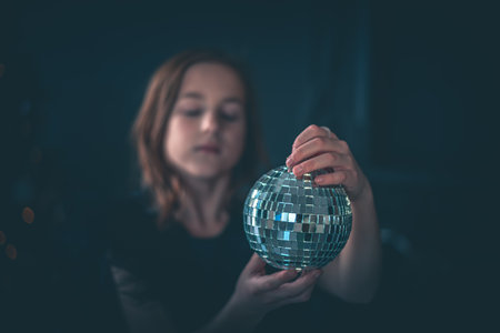 cute girl holds a disco ball against the background of a Christmas tree