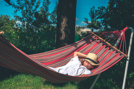 The girl lies on a hammock covering her face with a hat outdoors. relax, vacation, summer holidaysの写真素材