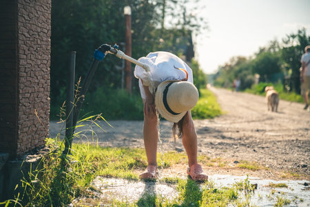 Cute girl in the village drinking tap water, country lifeの写真素材