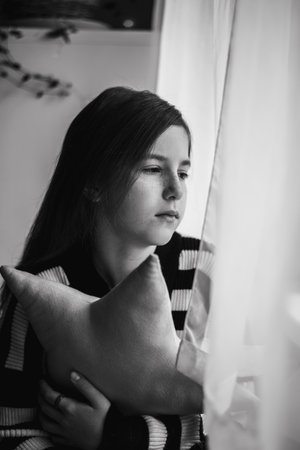 A thoughtful teenage girl looks out the window. thoughtfulness, sadness, lonelinessの写真素材