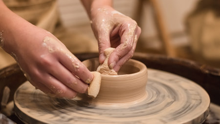 Potter girl works on potter's wheel, making ceramic pot out of clay in pottery workshop. Art and hobby conceptの写真素材