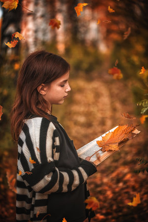girl with freckles with a book among autumn leaves. reading, magic autumn