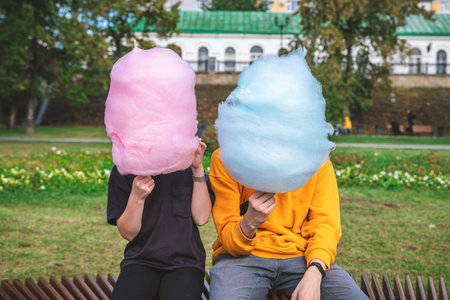 Two children are sitting with a large cotton candy blue and light blue. brother and sister, walk, childhood, sweets. without faceの写真素材