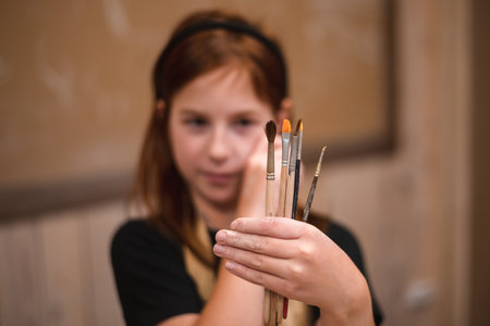 A girl in a creative workshop holds brushes for coloring a clay productの写真素材