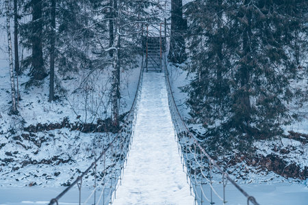 Beautiful rope hanging wooden bridge over the river. winter landscape, snow-covered forest. perspective, symmetryの写真素材