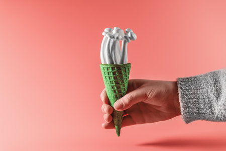 hand holding a bunch of shimeji mushrooms with green moss in green ice cream cone, on pink background, superfood, a type of delicious oyster mushroom, healthy foodの写真素材