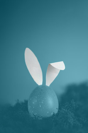 Tinted in blue photo, easter egg with white rabbit ears. creative minimalistic photo with copy space