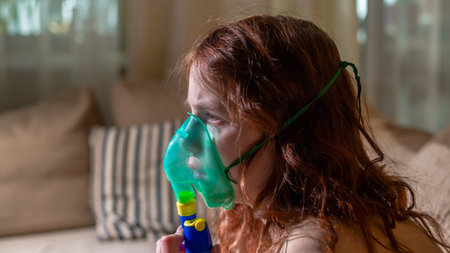 Sick girl making inhalation with nebulizer to reduce coughing, at home, child taking medication while breathing in through face mask. Bronchitis and asthma treatments for childrenの写真素材