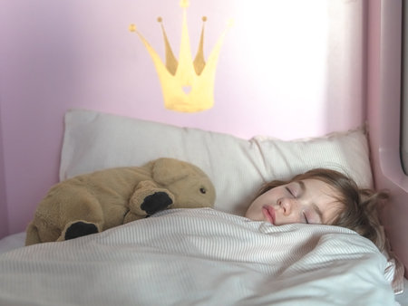 cute little girl sleeps in bed with soft toyの写真素材
