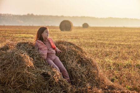 Cute teenage girl in field with wheat clippings and haystacks. morning, fog