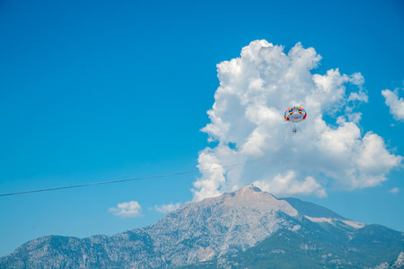 Two people parasailing on a colorful parachute flying against the background of mountains, blue sky and cloudsの写真素材