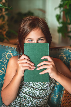 cute teenage girl with red hair and brown eyes smiling and holding green book in front of her, concept learning, reading, joyの写真素材