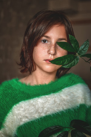Portrait of a cute teenage girl with freckles in a green sweater and with a green leaf of a house plantの写真素材