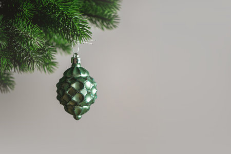 Christmas tree toy in the shape of a green pine cone hanging from a christmas tree branch on gray background representing christmas and new year, with copy spaceの写真素材