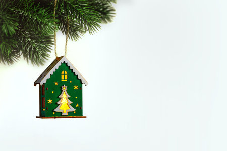 Christmas tree toy in the form of a house with glowing windows hanging from a christmas tree branch on white background representing christmas and new year, with copy spaceの写真素材