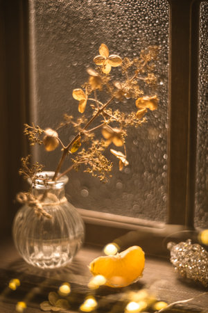 Warm sunlight illuminates a glass vase containing dried hydrangea flowers and tangerine, orange slices, creating a cozy winter scene on a windowsillの写真素材